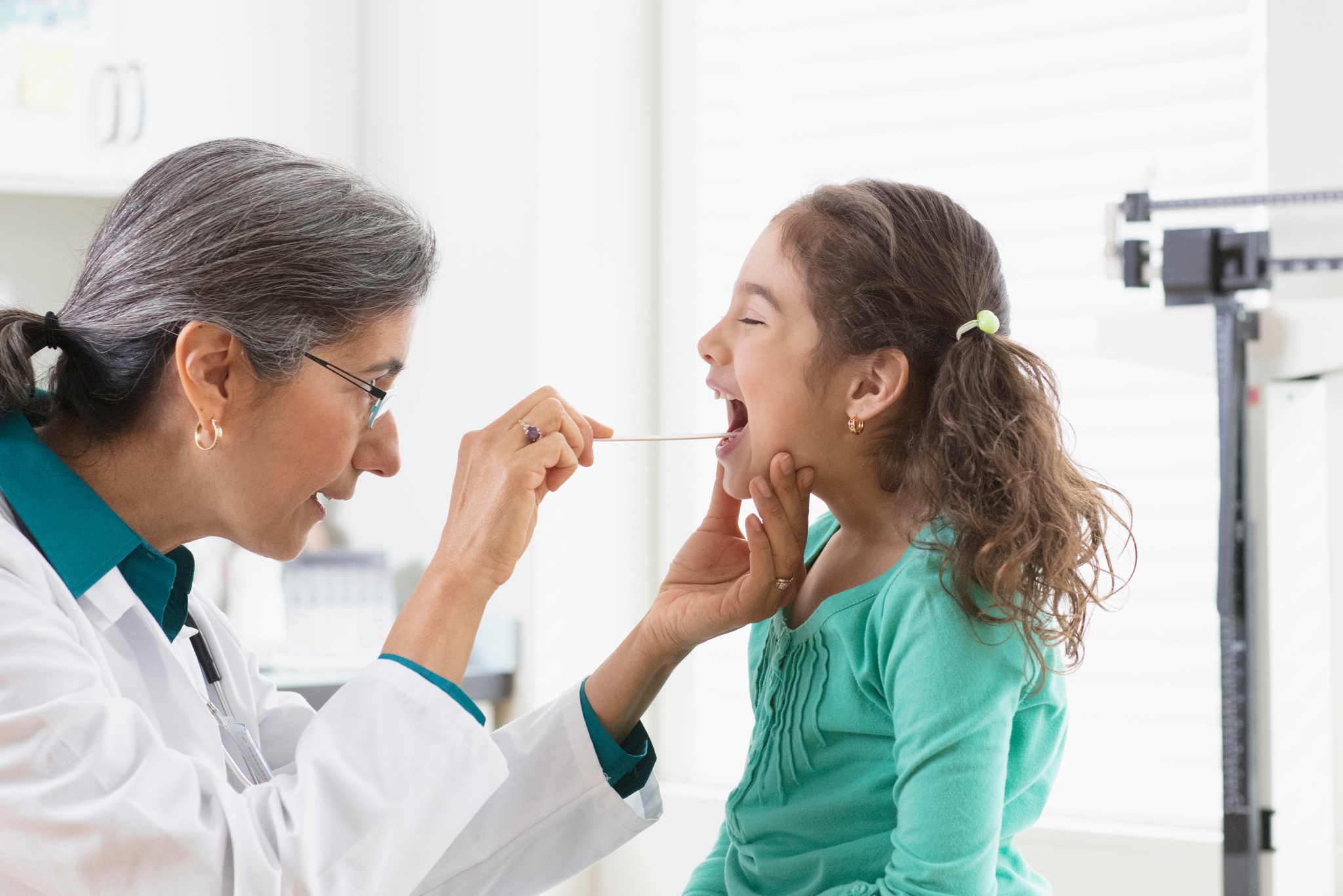 Senior doctor examining young girl throat at clinic
